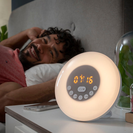 Réveil lumineux simulateur d'aube blanc allumé sur une table de nuit